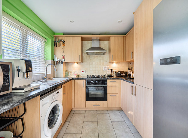 Fitted kitchen with integrated oven, hob and window above the sink.