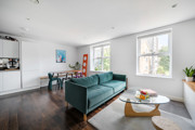 Open-plan living room with a teal sofa, dining table and large windows.