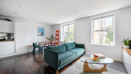 Open-plan living room with a teal sofa, dining table and large windows.