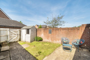 Backyard with paved area with small table and 2 chairs, grass patch, and garden shed.