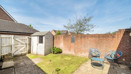 Backyard with paved area with small table and 2 chairs, grass patch, and garden shed.