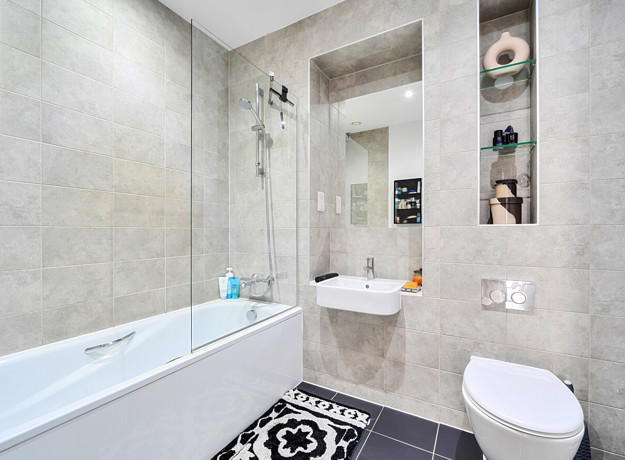 Bathroom with shower over bath, sink, toilet and bathmat on the floor.