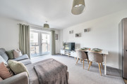 Open-plan living and dining area with sofa, dining table and balcony doors.