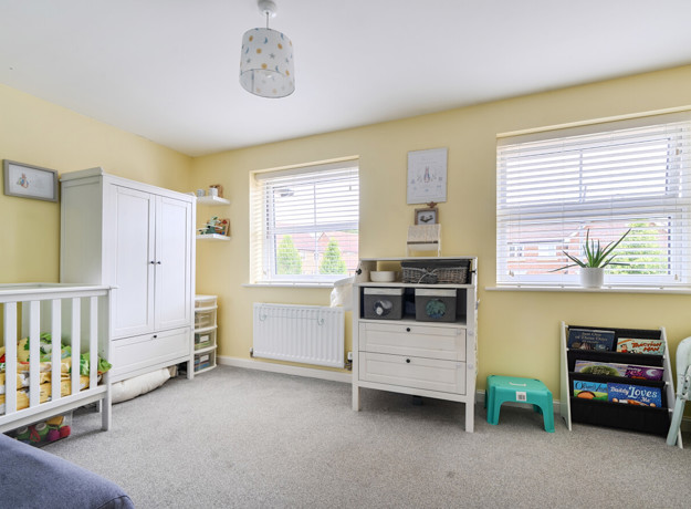 Nursery room with cot, storage units, yellow walls and window.