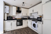 Fitted white kitchen with appliances, dark worktops and wood-effect flooring.