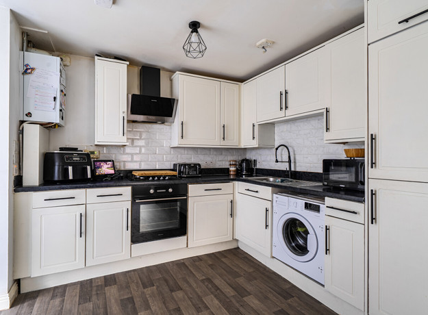 Fitted white kitchen with appliances, dark worktops and wood-effect flooring.