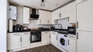Fitted white kitchen with appliances, dark worktops and wood-effect flooring.