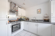 White fitted kitchen with integrated oven, hob and tiled flooring.