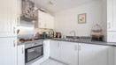 White fitted kitchen with integrated oven, hob and tiled flooring.