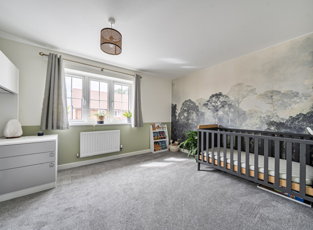 Bedroom with cot, chest of drawers, window and feature wall.