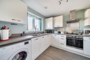 White fitted kitchen with integrated appliances and wood-effect flooring.