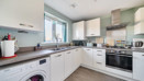 White fitted kitchen with integrated appliances and wood-effect flooring.