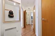 Hallway with wooden floor, framed wall art, doors, and wall heater.