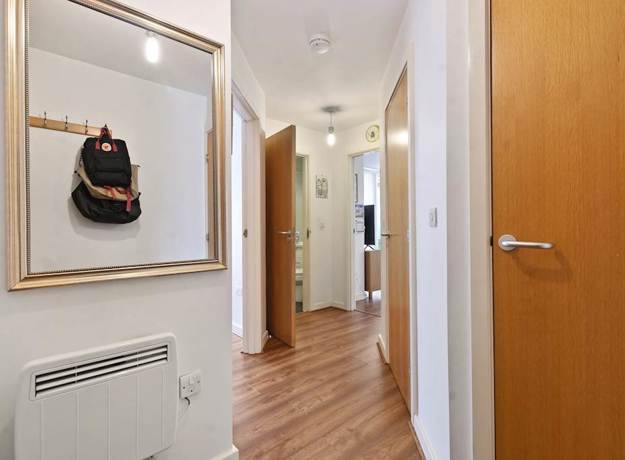 Hallway with wooden floor, framed wall art, doors, and wall heater.