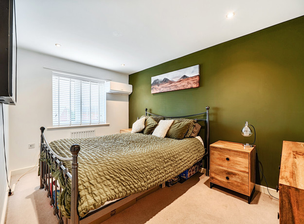 Bedroom with green feature wall, double bed, bedside tables and window.