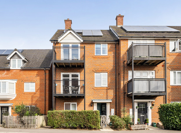 Apartment building with balconies, brick façade and landscaped frontage.