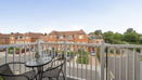 Balcony with outdoor table and chairs overlooking nearby buildings and rooftops.