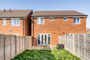 Rear view of a red-brick house with fenced garden and patio doors.