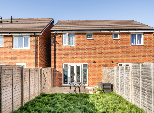 Rear view of a red-brick house with fenced garden and patio doors.