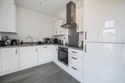 Kitchen with white cabinets, oven, hob, sink and appliances along walls.