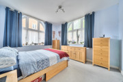 Bedroom with double bed, blue bedding, wooden dresser and cabinets with drawers, and large windows.