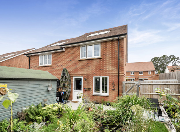 Rear view of semi-detached red brick house with garden and patio doors.