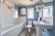 Bathroom with bathtub, toilet, sink, wood-effect flooring and blue painted walls.