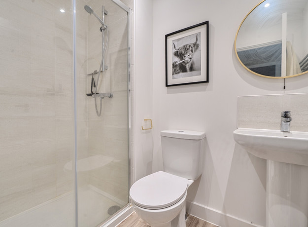 Ensuite with glass shower, toilet, sink, and round mirror.