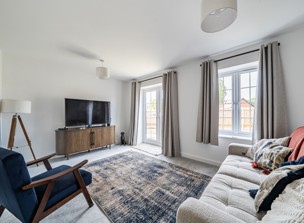 Living room with sofa, TV, rug, window and patio doors with curtains.