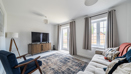 Living room with sofa, TV, rug, window and patio doors with curtains.
