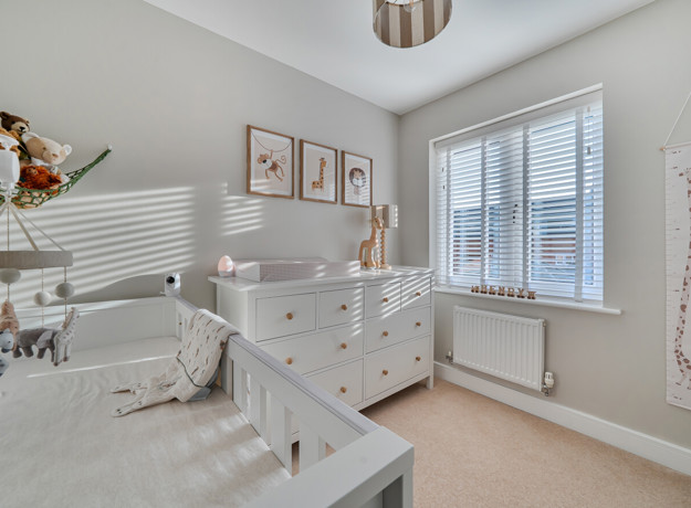 Bedroom with a cot, chest of drawers and window with blinds.