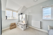 Bedroom with shelving unit, radiator and windows on two walls.