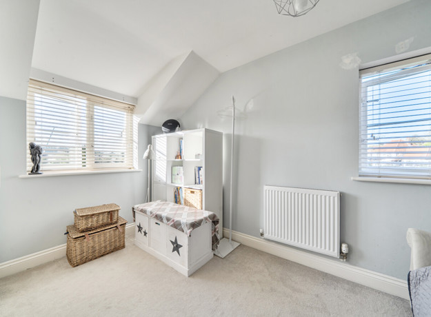 Bedroom with shelving unit, radiator and windows on two walls.