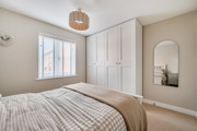 Bedroom with fitted wardrobes, wall mirror and window with blinds.