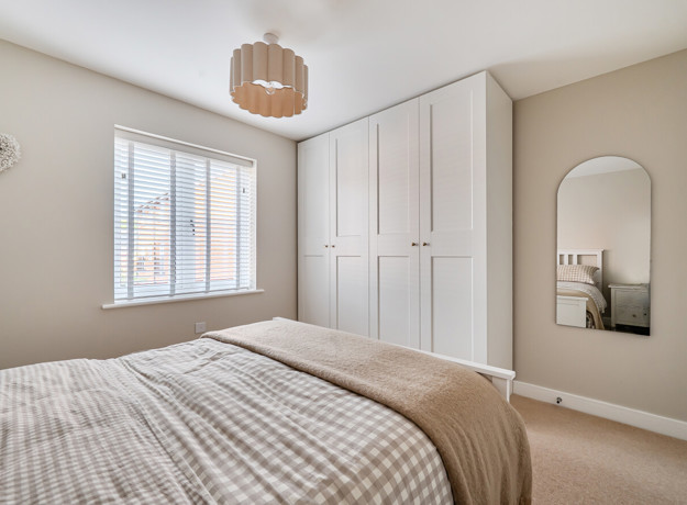 Bedroom with fitted wardrobes, wall mirror and window with blinds.
