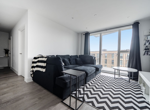 Open-plan living area with corner sofa, patterned rug and balcony doors.