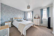 Bedroom with double bed, bedside tables, chest of drawers and two windows.