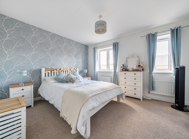 Bedroom with double bed, bedside tables, chest of drawers and two windows.