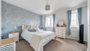 Bedroom with double bed, bedside tables, chest of drawers and two windows.