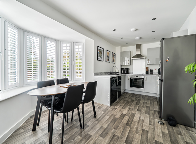 Open-plan kitchen and dining area with table, chairs and window blinds.