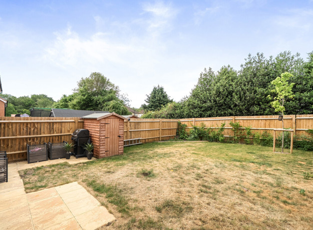 Back garden with grass lawn, wooden fence, shed, and surrounding trees.