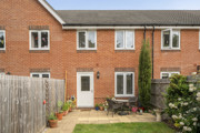 Rear view of a red brick terraced house with small patio and plants.