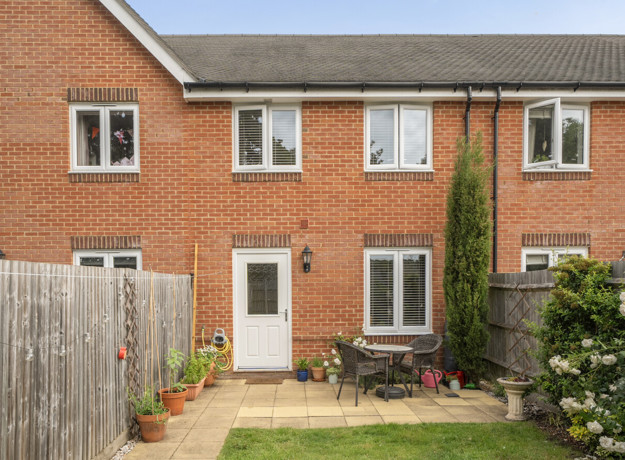 Rear view of a red brick terraced house with small patio and plants.