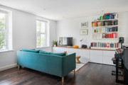 Living area with a teal sofa, wall-mounted shelves, piano and windows.