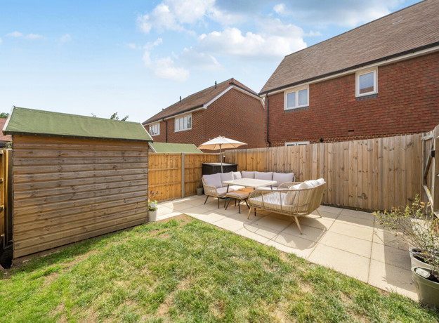 Small garden with lawn, shed, patio seating, and fenced boundaries.