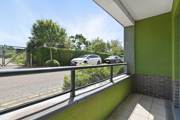 Balcony with railing, green wall detail, and view of street and trees.