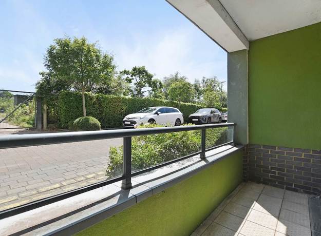 Balcony with railing, green wall detail, and view of street and trees.