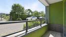 Balcony with railing, green wall detail, and view of street and trees.