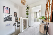 Landing with framed artwork, staircase, radiator and carpeted door.