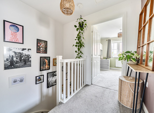 Landing with framed artwork, staircase, radiator and carpeted door.